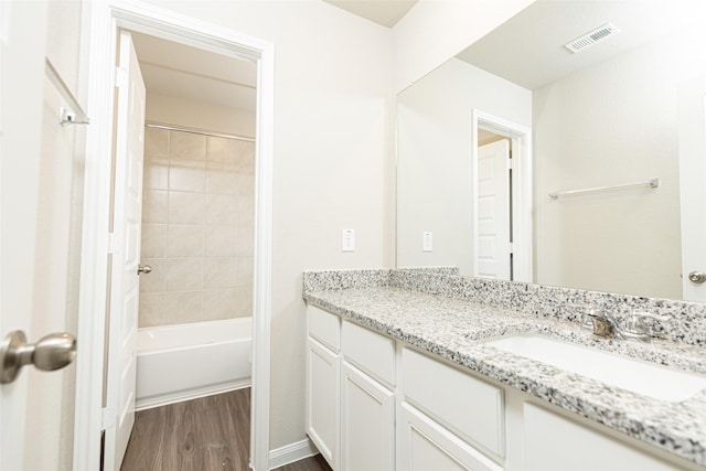 bathroom featuring wood-type flooring, tiled shower / bath, and vanity