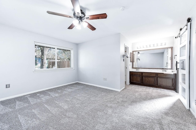 unfurnished bedroom featuring ensuite bathroom, ceiling fan, sink, a barn door, and carpet floors