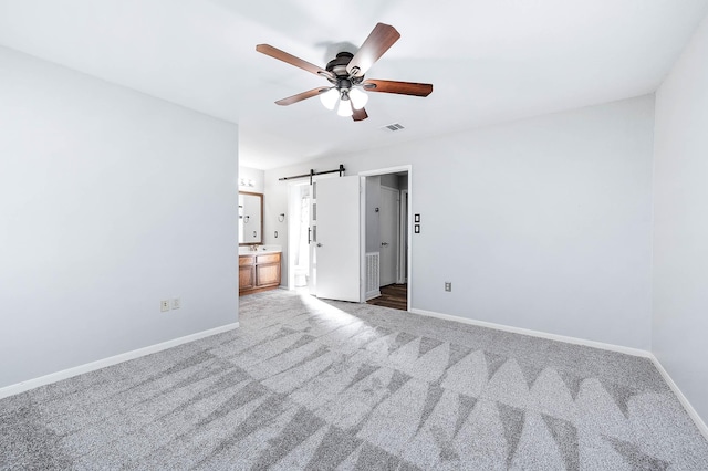 carpeted empty room featuring a barn door and ceiling fan