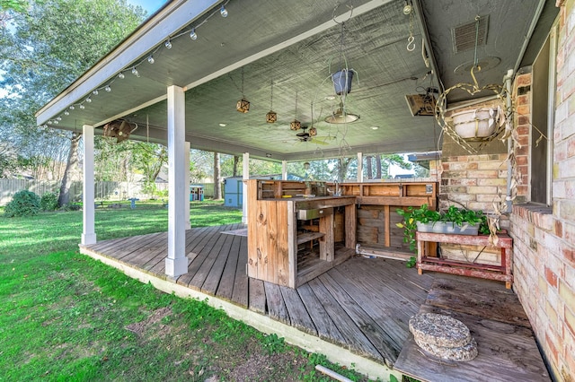 wooden terrace featuring ceiling fan, a storage unit, and a lawn