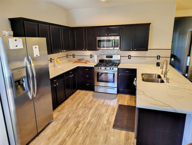 kitchen featuring light stone countertops, backsplash, stainless steel appliances, sink, and light hardwood / wood-style flooring