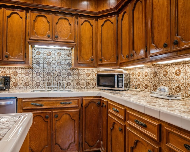 kitchen with appliances with stainless steel finishes, tasteful backsplash, tile counters, and sink