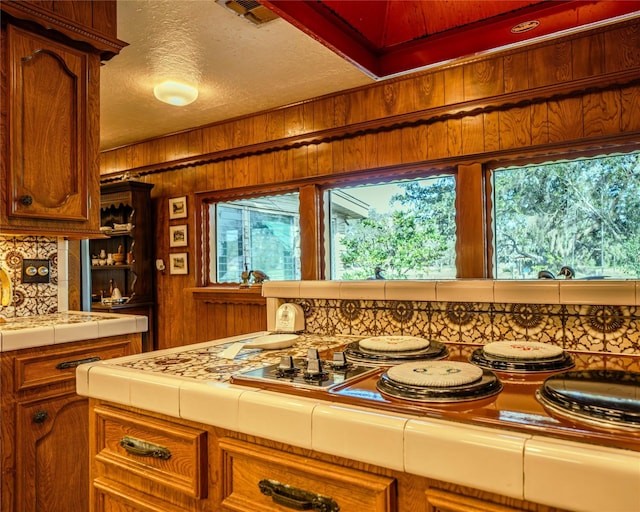 kitchen with a textured ceiling, tile counters, wood walls, and backsplash