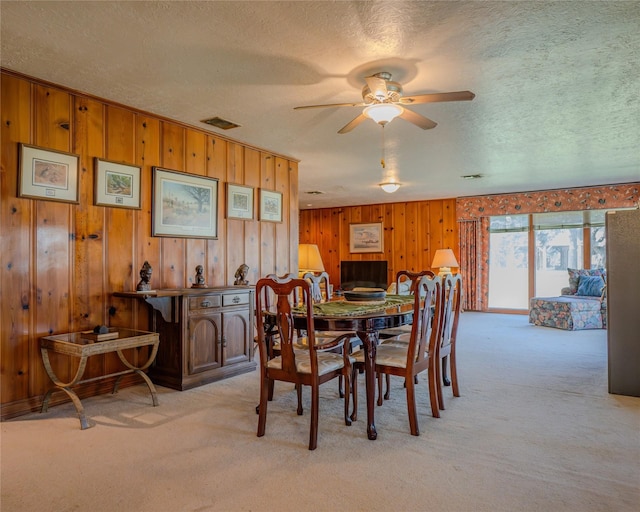 carpeted dining space featuring ceiling fan, wood walls, and a textured ceiling