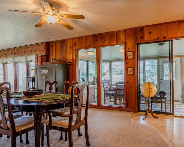 dining room featuring ceiling fan, a textured ceiling, and wooden walls