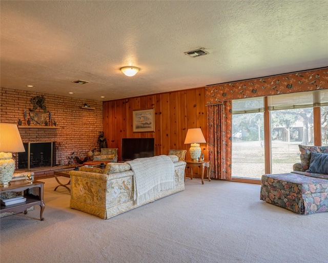 carpeted living room with wood walls, a textured ceiling, and a brick fireplace