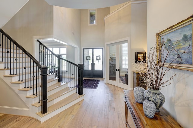 entrance foyer featuring french doors, a towering ceiling, light hardwood / wood-style flooring, and a healthy amount of sunlight