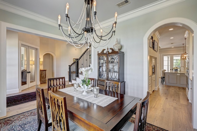 dining room featuring a chandelier, light wood-type flooring, crown molding, and french doors