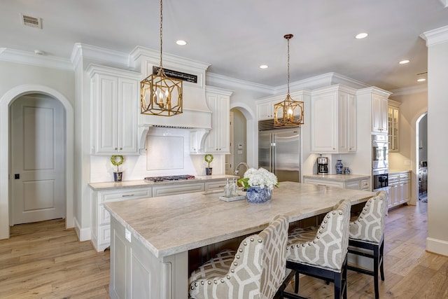 kitchen with a large island with sink, stainless steel appliances, and hanging light fixtures