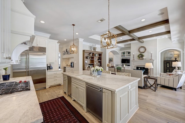 kitchen with light stone countertops, sink, beam ceiling, a center island with sink, and hanging light fixtures