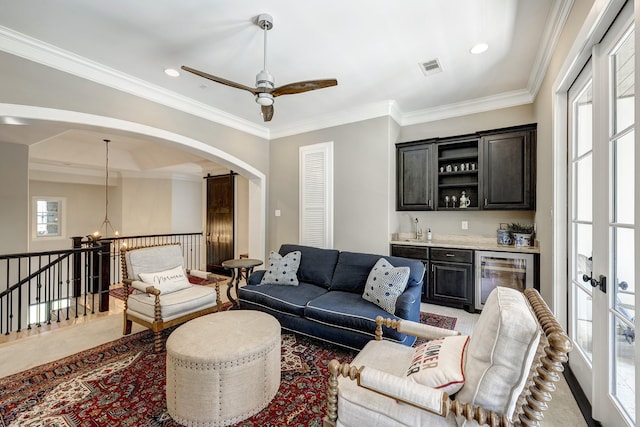 living room with bar area, wine cooler, ceiling fan with notable chandelier, and ornamental molding