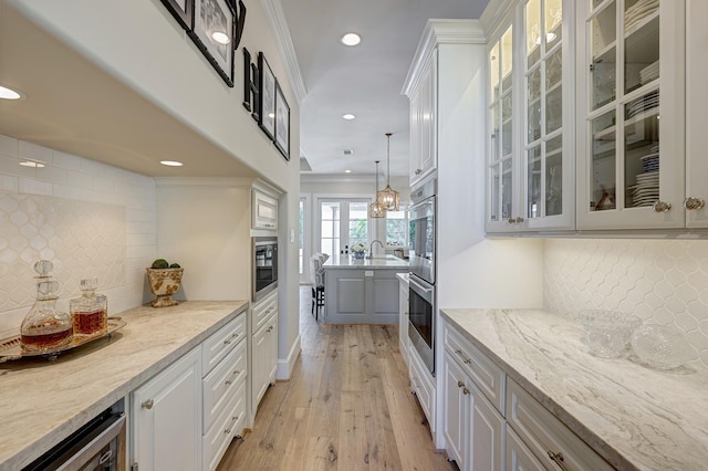 bar featuring decorative light fixtures, white cabinetry, light stone counters, and ornamental molding