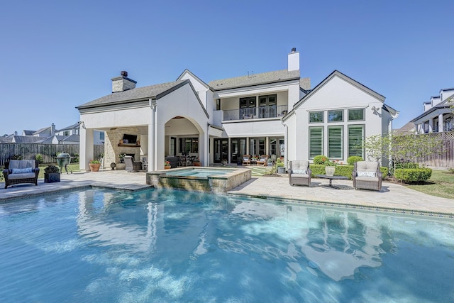 rear view of house with a fireplace, a swimming pool with hot tub, a patio, and a balcony