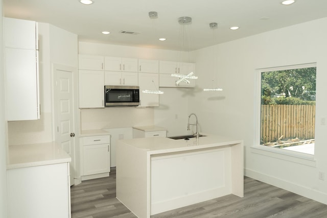 kitchen with a kitchen island with sink, white cabinets, sink, decorative light fixtures, and wood-type flooring