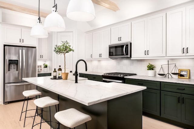 kitchen with a center island with sink, beam ceiling, white cabinets, and appliances with stainless steel finishes