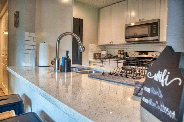 kitchen with sink, tasteful backsplash, light stone counters, white cabinets, and appliances with stainless steel finishes