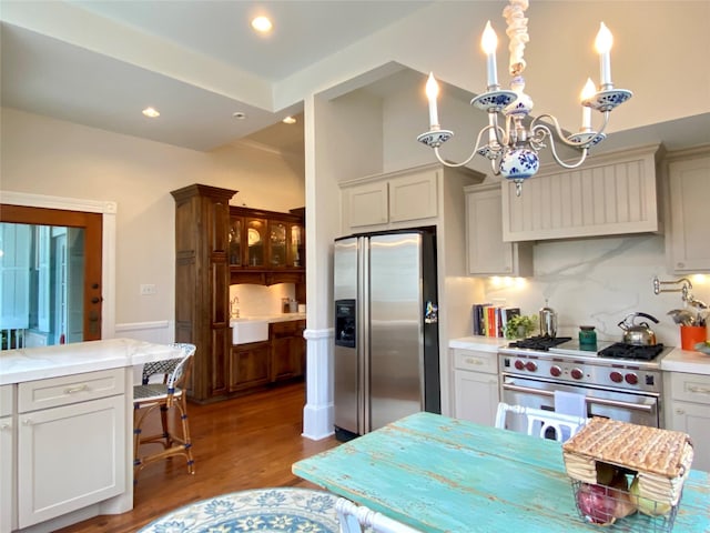 kitchen featuring backsplash, stainless steel appliances, decorative light fixtures, a notable chandelier, and hardwood / wood-style floors