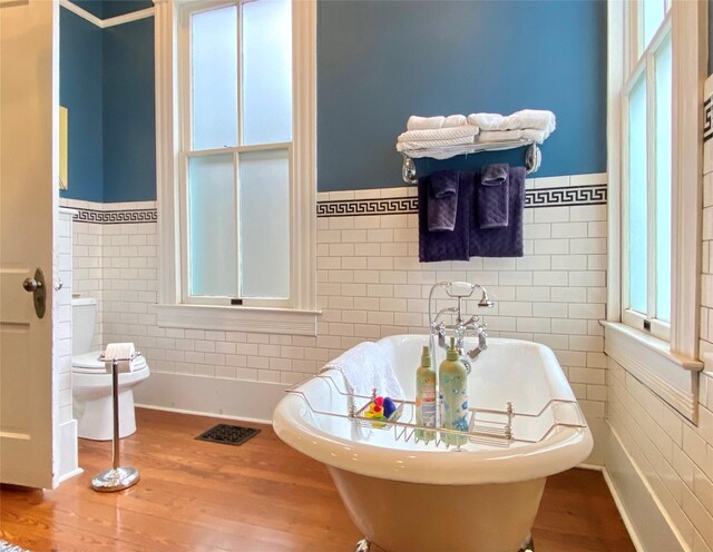 bathroom with a washtub, toilet, and tile walls