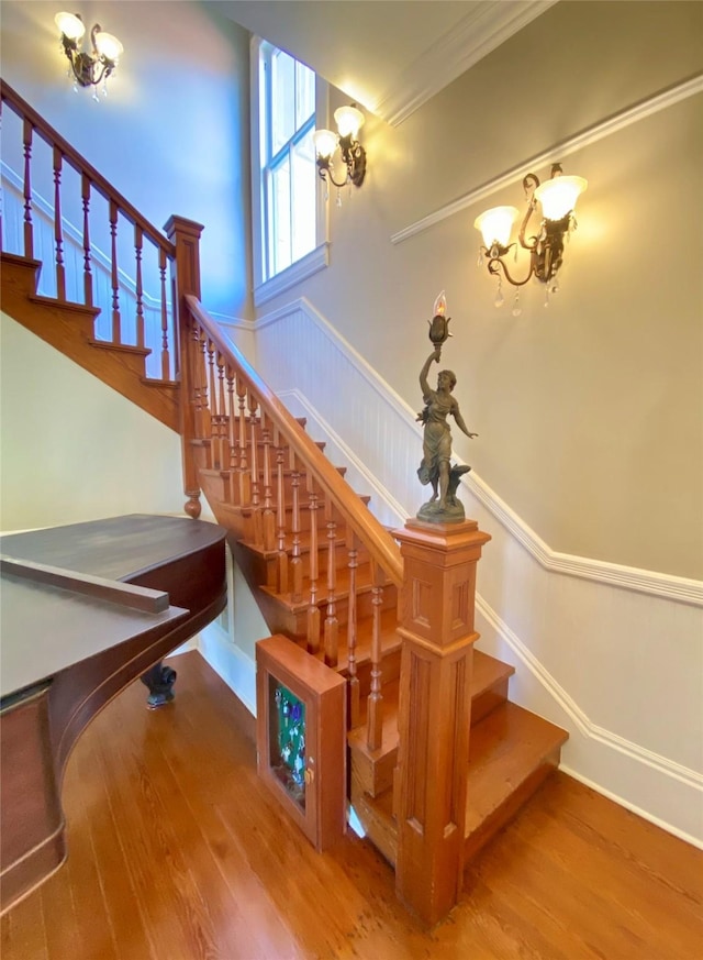 stairs featuring crown molding, hardwood / wood-style floors, and an inviting chandelier