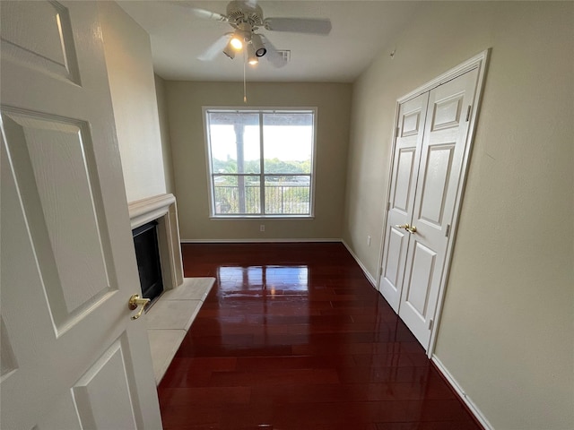 unfurnished living room featuring ceiling fan, a fireplace, and dark wood-type flooring