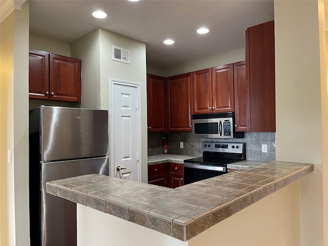 kitchen with backsplash, kitchen peninsula, tile countertops, and appliances with stainless steel finishes