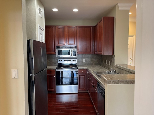 kitchen featuring sink, tasteful backsplash, dark hardwood / wood-style floors, kitchen peninsula, and appliances with stainless steel finishes