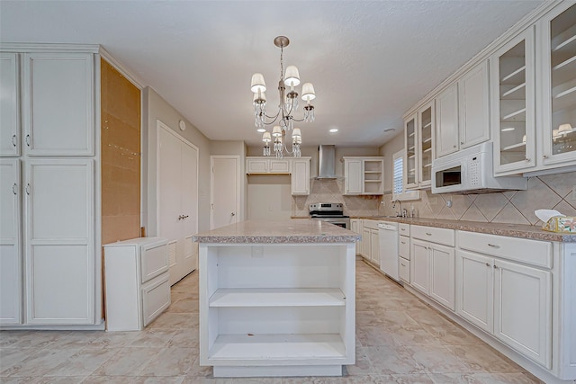 kitchen featuring white appliances, wall chimney exhaust hood, decorative light fixtures, a kitchen island, and a chandelier