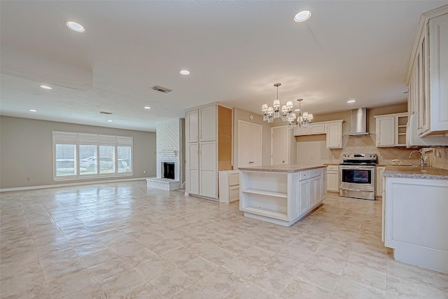 kitchen with wall chimney range hood, electric range, decorative light fixtures, a kitchen island, and a chandelier