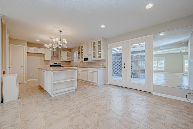 kitchen featuring french doors, wall chimney exhaust hood, stainless steel range with electric stovetop, decorative light fixtures, and a kitchen island