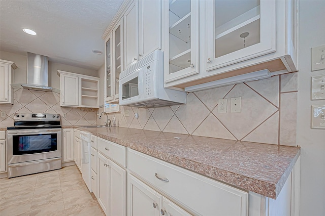 kitchen featuring stainless steel range with electric cooktop, wall chimney range hood, sink, light tile patterned floors, and white cabinetry