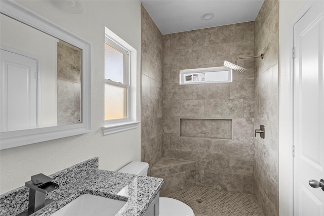 bathroom featuring a tile shower, vanity, and toilet