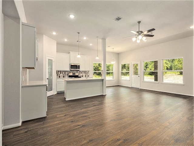 kitchen featuring appliances with stainless steel finishes, ceiling fan, a center island with sink, decorative light fixtures, and dark hardwood / wood-style floors