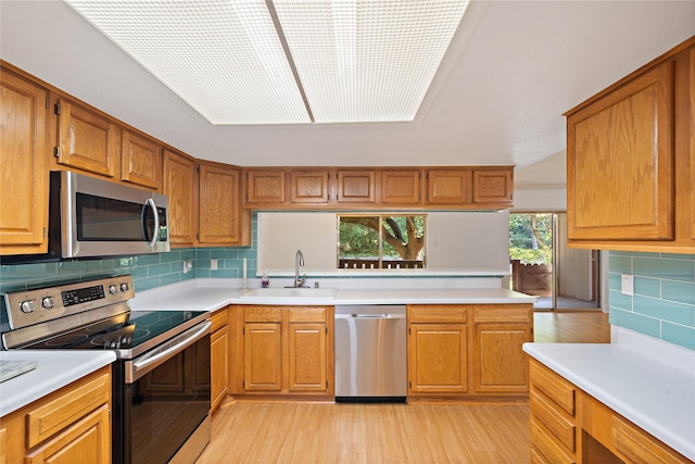 kitchen featuring sink, light hardwood / wood-style flooring, backsplash, kitchen peninsula, and appliances with stainless steel finishes