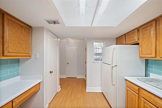 kitchen featuring white refrigerator, light wood-type flooring, and backsplash