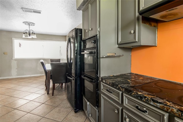 kitchen with pendant lighting, dark stone counters, black appliances, light tile patterned floors, and a textured ceiling