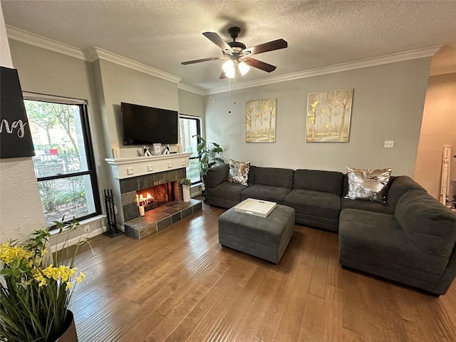 living room with hardwood / wood-style flooring, ceiling fan, ornamental molding, a textured ceiling, and a fireplace