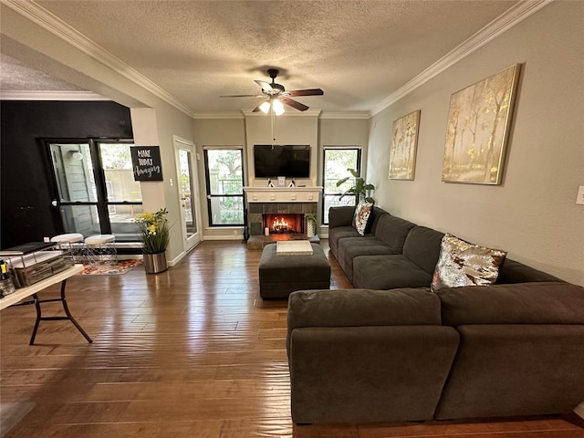 living room featuring ceiling fan, hardwood / wood-style floors, a textured ceiling, a fireplace, and ornamental molding