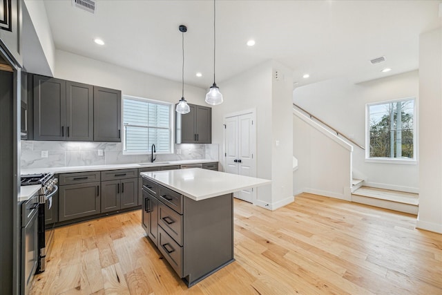 kitchen featuring hanging light fixtures, stainless steel range with gas cooktop, a kitchen island, decorative backsplash, and sink