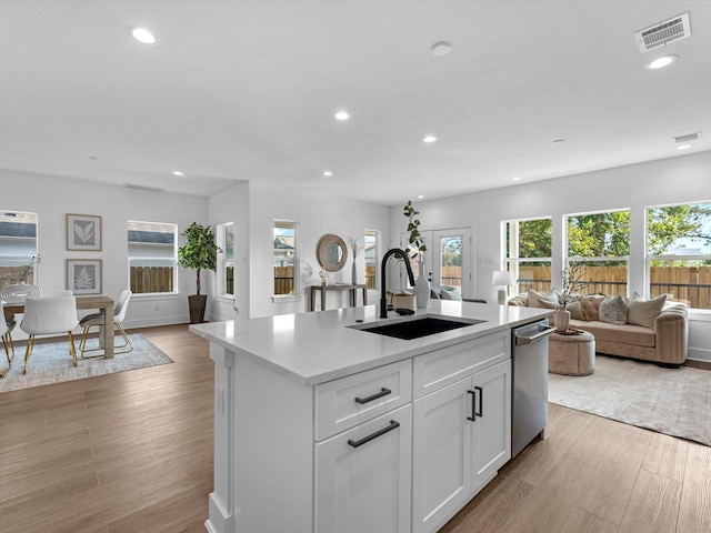 kitchen with stainless steel dishwasher, sink, white cabinetry, plenty of natural light, and an island with sink