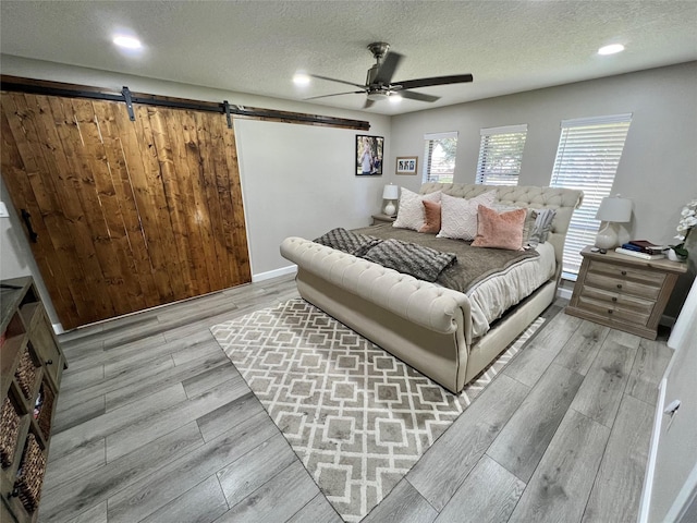 bedroom with ceiling fan, a barn door, light wood-type flooring, and a textured ceiling