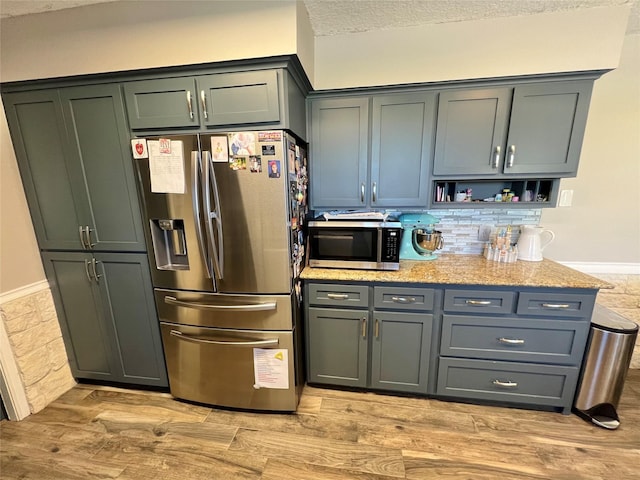 kitchen featuring light stone counters, a textured ceiling, appliances with stainless steel finishes, and light hardwood / wood-style flooring