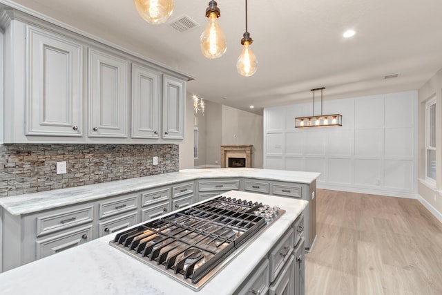 kitchen featuring gray cabinetry, stainless steel gas stovetop, hanging light fixtures, and light hardwood / wood-style flooring