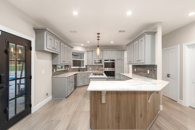 kitchen featuring pendant lighting, decorative backsplash, gray cabinets, kitchen peninsula, and stainless steel appliances