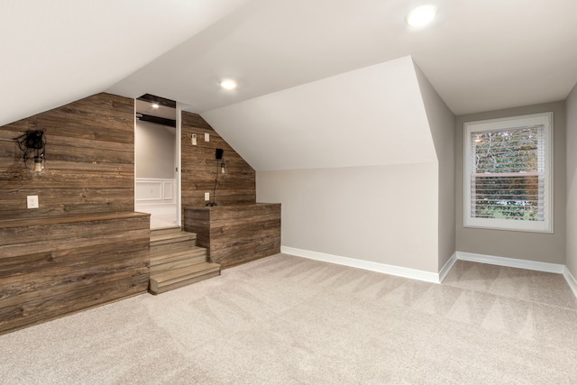 bonus room with carpet flooring, lofted ceiling, and wooden walls