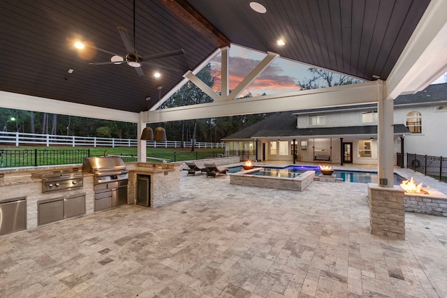 patio terrace at dusk with ceiling fan, an outdoor kitchen, a fire pit, a gazebo, and area for grilling