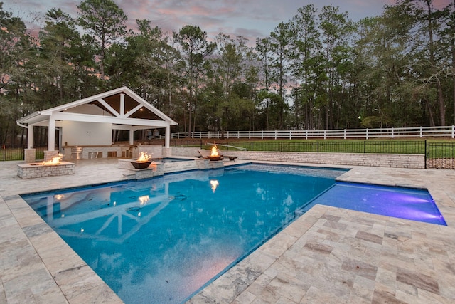 pool at dusk featuring a patio area and an outdoor fire pit