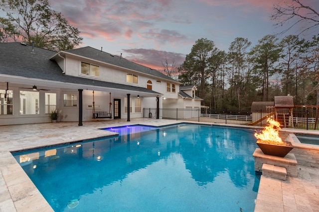 pool at dusk with a patio area, ceiling fan, and a fire pit