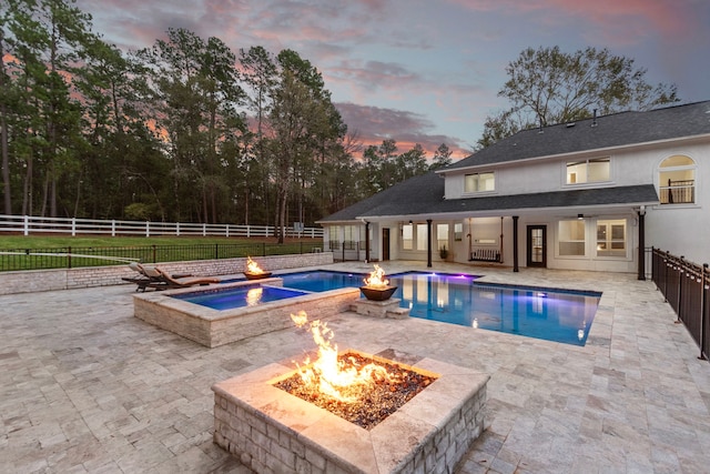 pool at dusk with a patio area, an in ground hot tub, and an outdoor fire pit