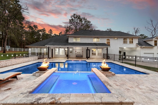 pool at dusk featuring an in ground hot tub, a patio, a fire pit, and ceiling fan