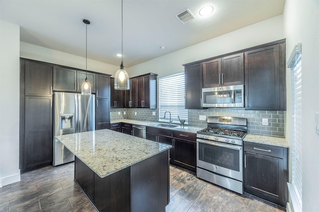 kitchen with light stone countertops, sink, a center island, hanging light fixtures, and appliances with stainless steel finishes